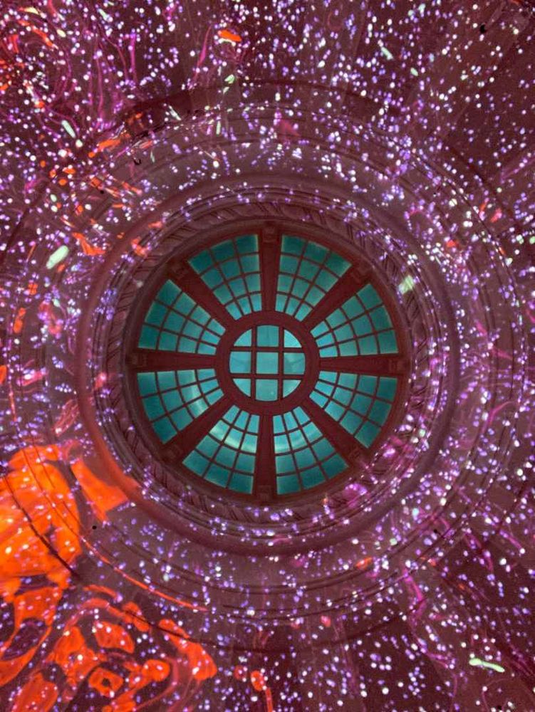 Looking up at a multicolored light installation projected on the inside of a dome, swirling reds against white spotted purple with the dome window green.