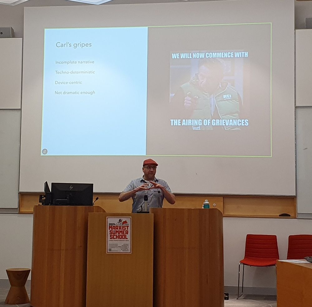 Carl presenting at a seminar. Screen behind him has a picture of Frank Constanza that reads "We will now commence with the airing of grievances"