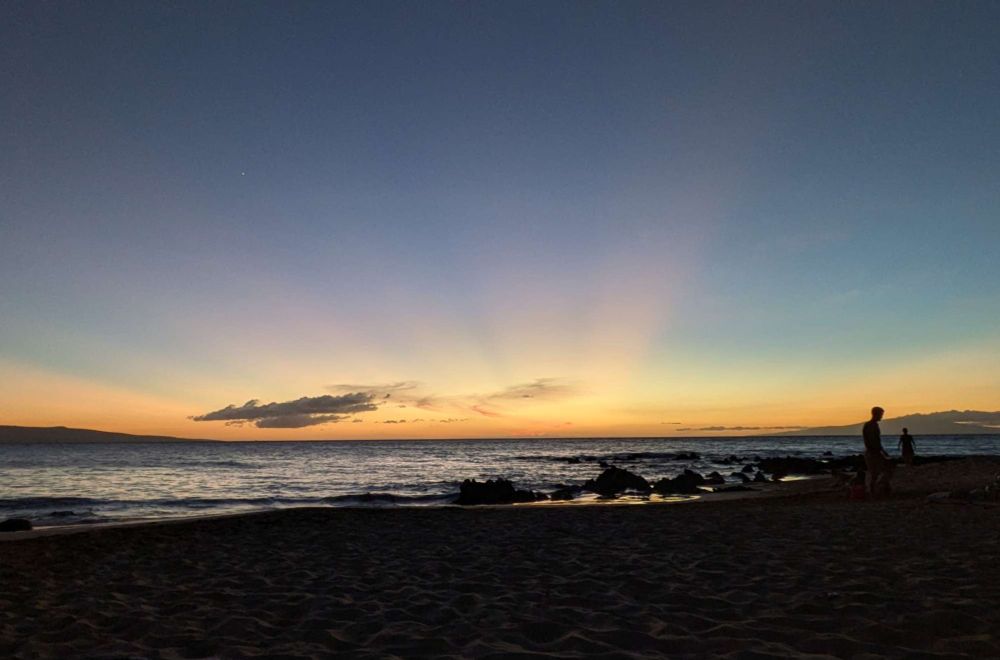 sunset on an ocean beach, orange and yellow along the horizon with pink rays shooting up.