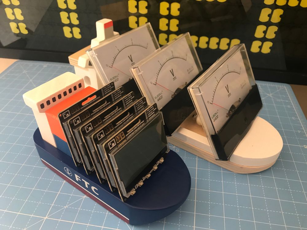 5 Pimoroni GFX pack displays are pictured on a small wooden container ship toy next to a larger wooden container ship which has 3 Adafruit analog gauges on it.