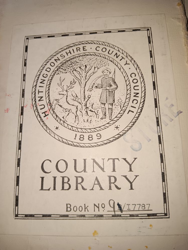 A book plate in a library book with the round Huntingdonshire County Council logo with a tree, a stag and a hunter in the middle and 1889 on the bottom. Below says County Library