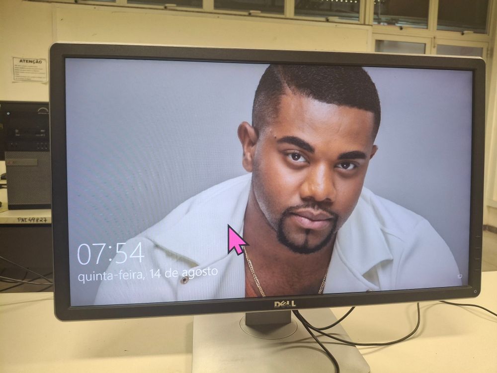 Um monitor na tela de bloqueio do Windows com uma foto do Davi Brito de wallpaper e um cursor rosa comicamente grande.