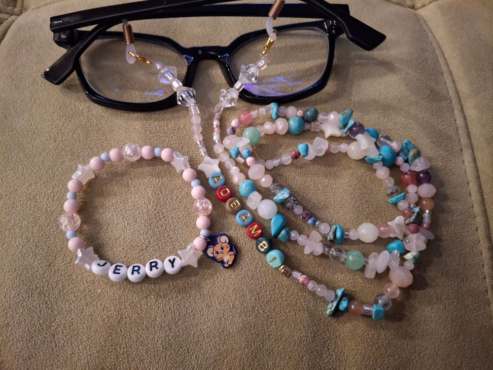 The previously mentioned glasses chain next to the friendship bracelet that inspired it, it says "Jerry" in white alphabeads and the rest is composed of plastic beads in white, pink, and periwinkle. There is a small charm depicting Jerry the mouse of Tom and Jerry fame.