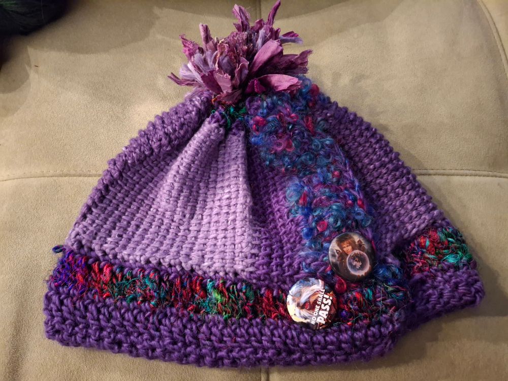 A hat made from two different purple wool and silk blend yarns--one gradient and one solid, two different textures of yarn made from recycled sari scraps, and a stripe of multicolored curly texture novelty yarn.  There are two pins on it depicting images from the film the Labyrinth (I did not make these pins).  This took me years to start and several days to finish.