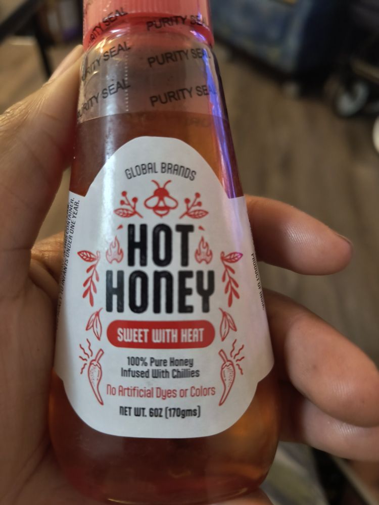 In the picture is a hand holding a bottle of hot honey. It is advertised on the bottle as sweet with heat, and says it's 100% pure honey infused with chilies
