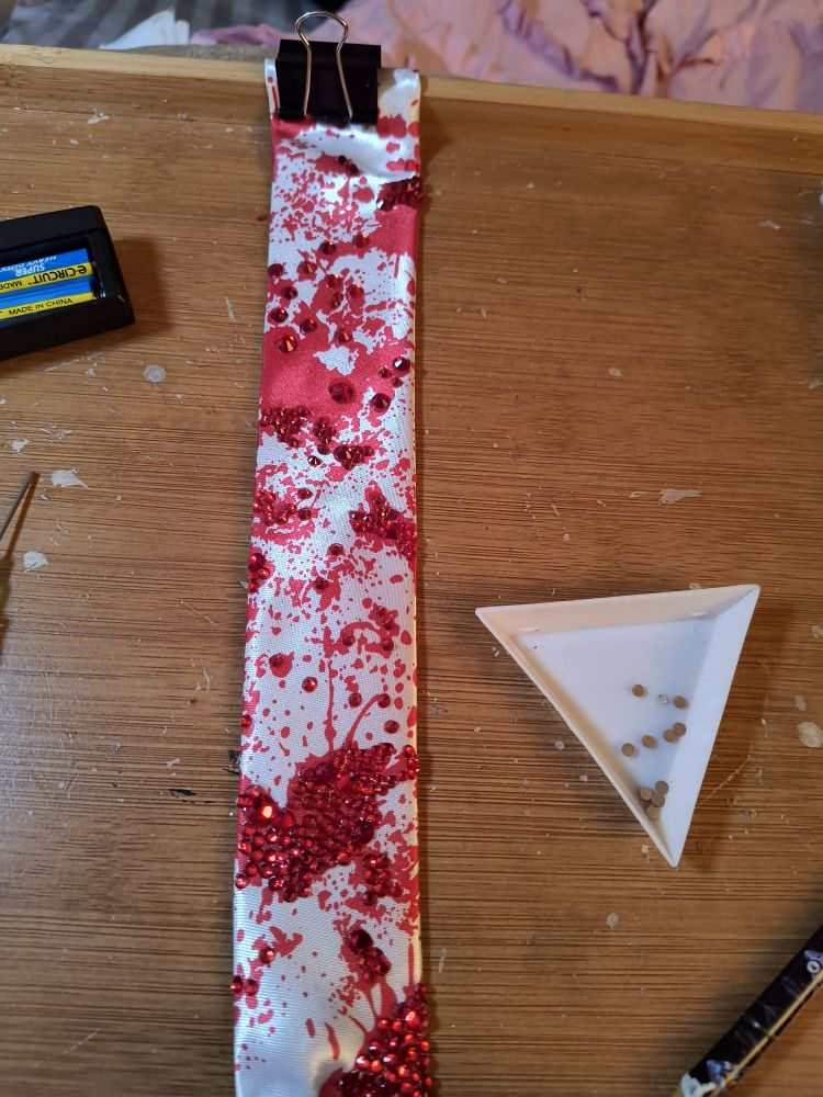 In the picture is a shiny white tie with simulated blood spatters embellished with red rhinestones.