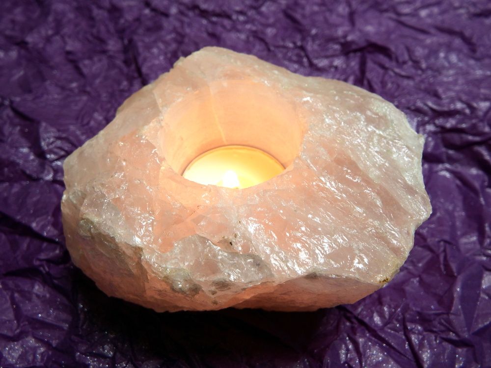 A rough pink stone (rose quartz) candle holder with a lit candle on a purple background.