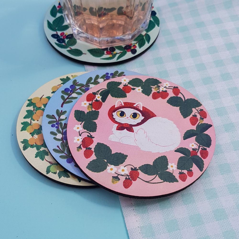 a set of 4 coasters depicting cats in babushka scarves surrounded by berry plants - only the top one is fully visible: it's a pink coaster with white cat in a red head scarf with strawberry plants around. the other coasters have blueberries, blackberries and gooseberries on them.
