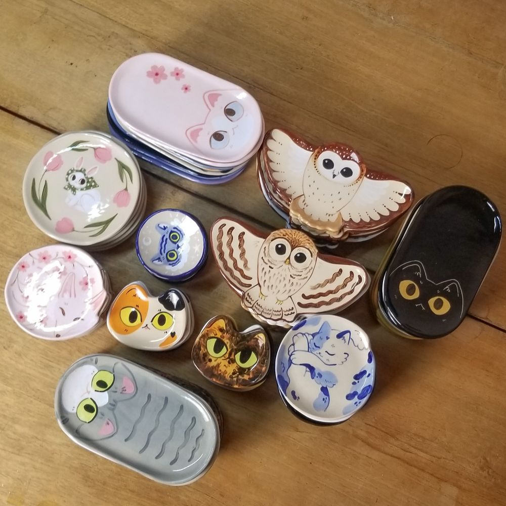 stacks of small ceramic plates shaped like cats, owls and foxes lying on a table
