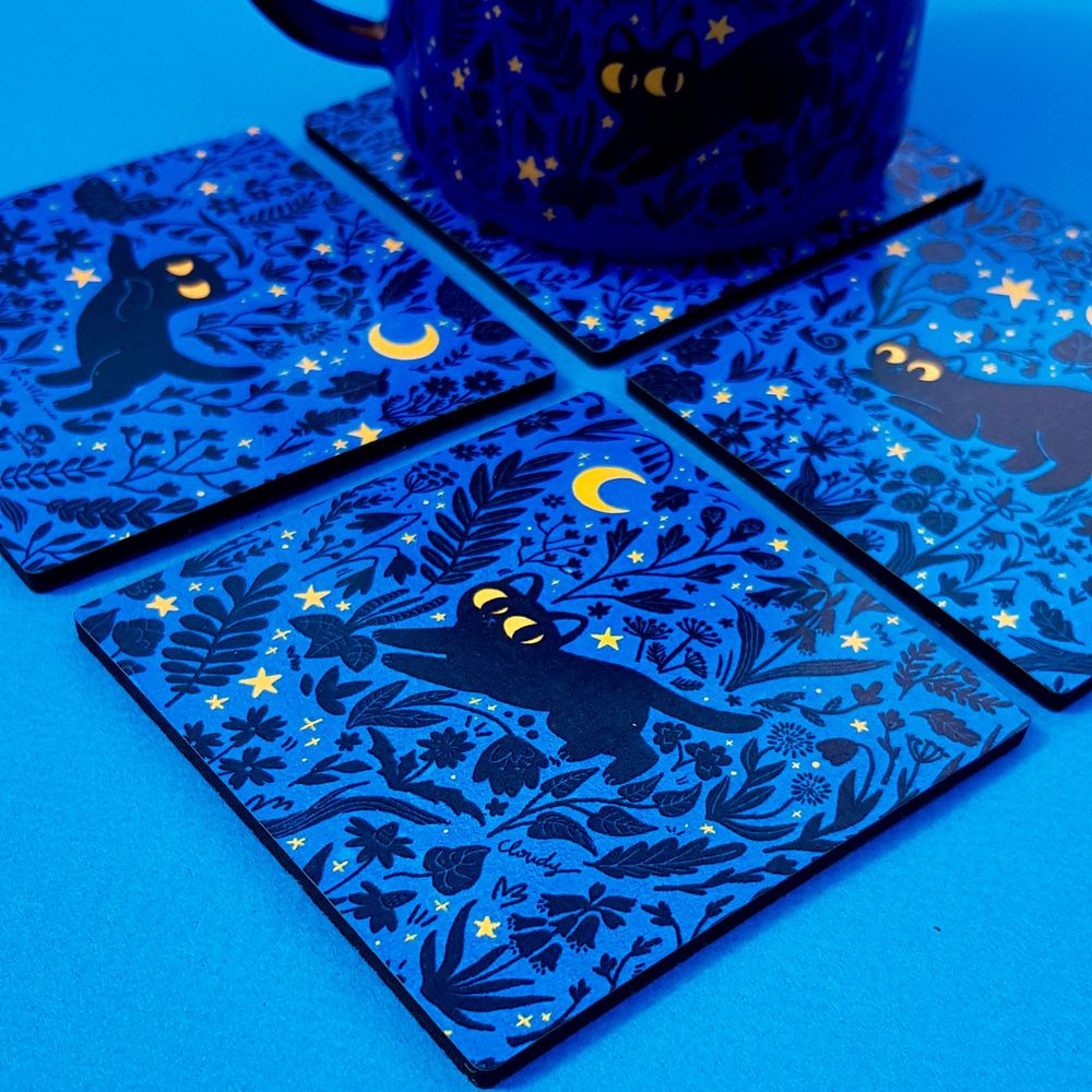 a set of 4 blue coasters with images of black cats in the night surrounded by plant silhouettes and yellow stars
