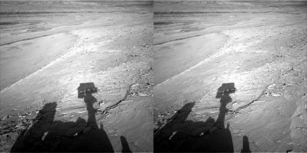 A dual left/right stereoscopic pair of black and white photographies displaying a Martian landscape and the shadow of the Curiosity rover. This dual image is intended to be used to obtain a Stereo3D rendition of the scene through parallel viewing, and not cross-eyed viewing.