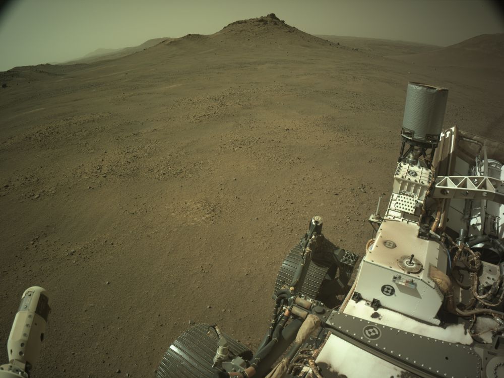 An ochre-toned image capturing a Martian landscape, with the rover in the foreground. 