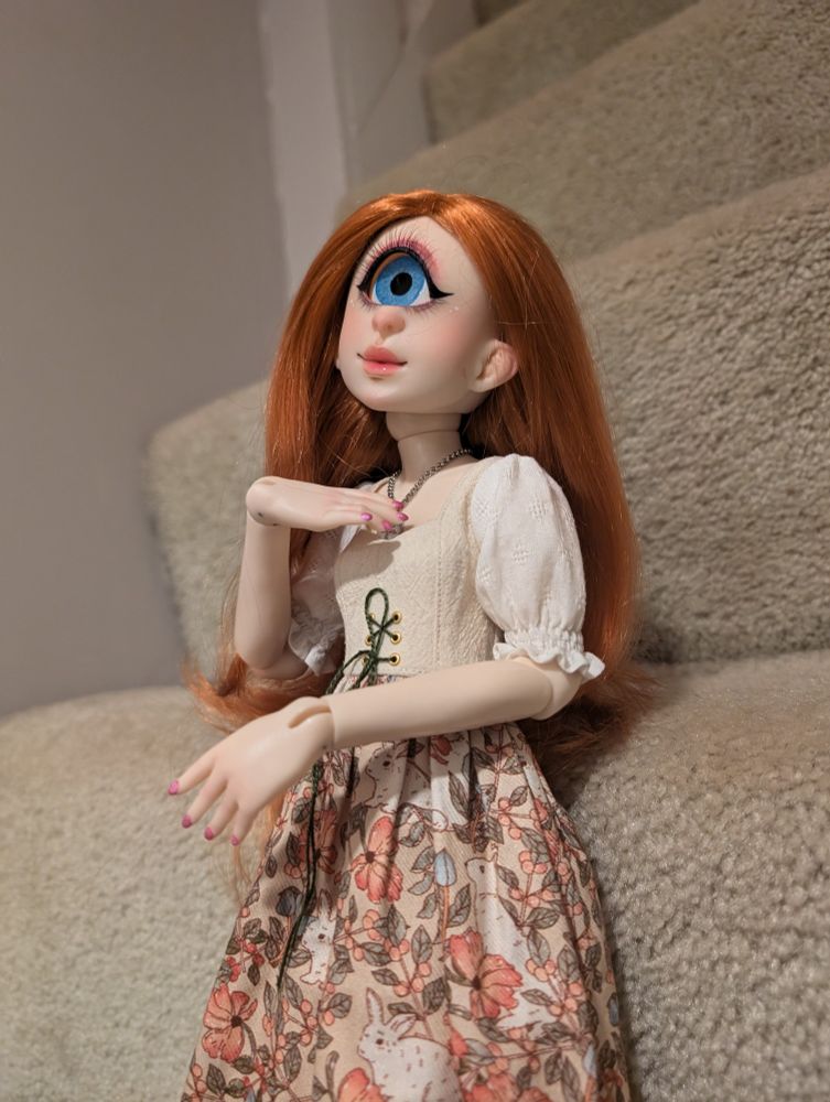 A cyclops ball jointed doll with silky long red hair and a cream and pink cottagecore style dress