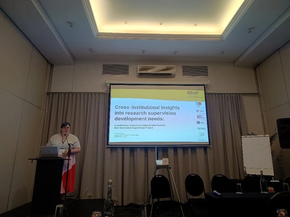 Image of Liz Quinlan standing at a lectern with a presentation slide in the background which says "Cross-institutional insights into research supervision development needs."