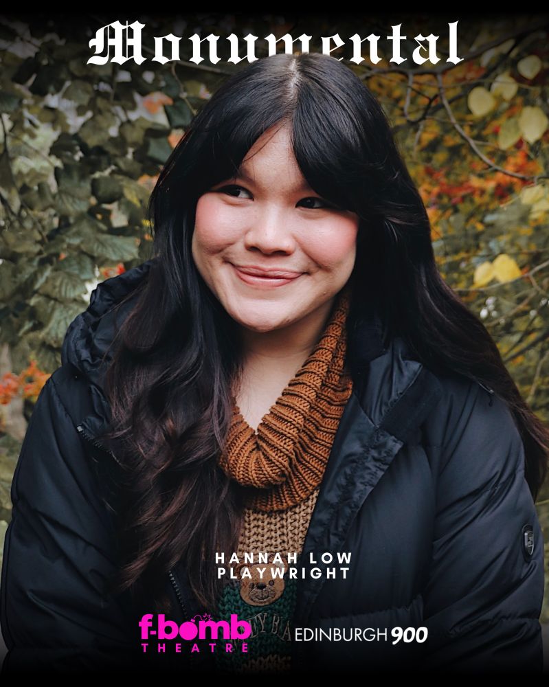 Photo of Hannah Low. She has long black hair, is wearing a black jacket and brown jumper, smiling. The background is autumn trees. 