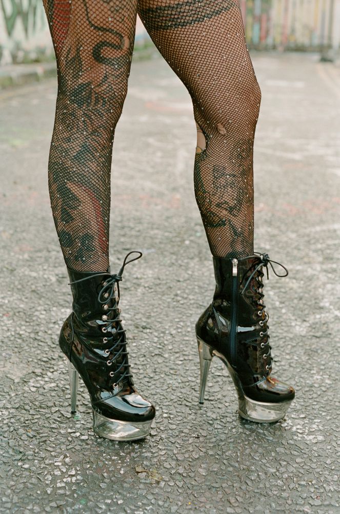 A photo of SJ's tattooed legs as she wears ripped fishnet stockings and shiny black high heeled boots.