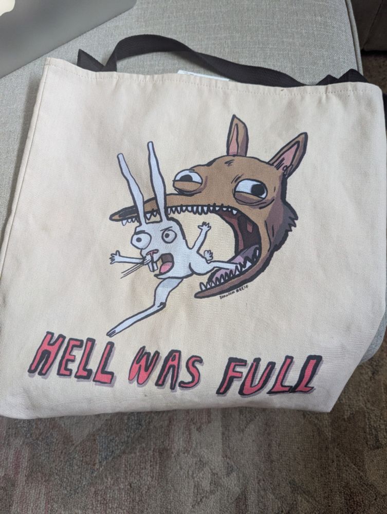 A tote bag with a Branson Reese image of a rabbit leaping from the mouth of a coyote with the caption "Hell way full."