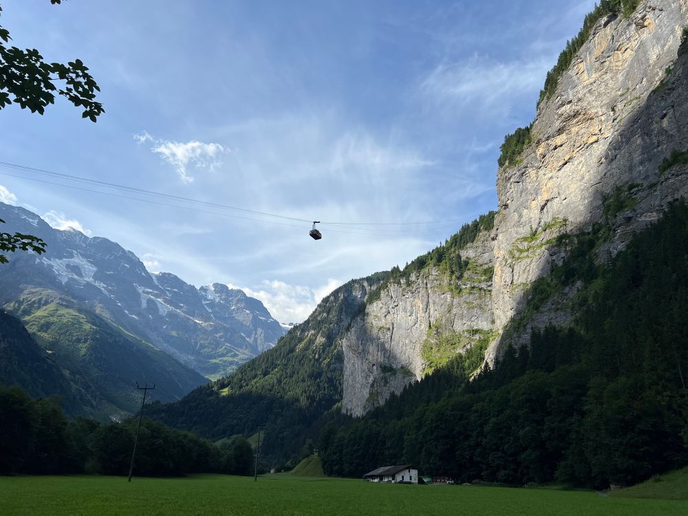 Gondola above snowy peaks and a green valley 