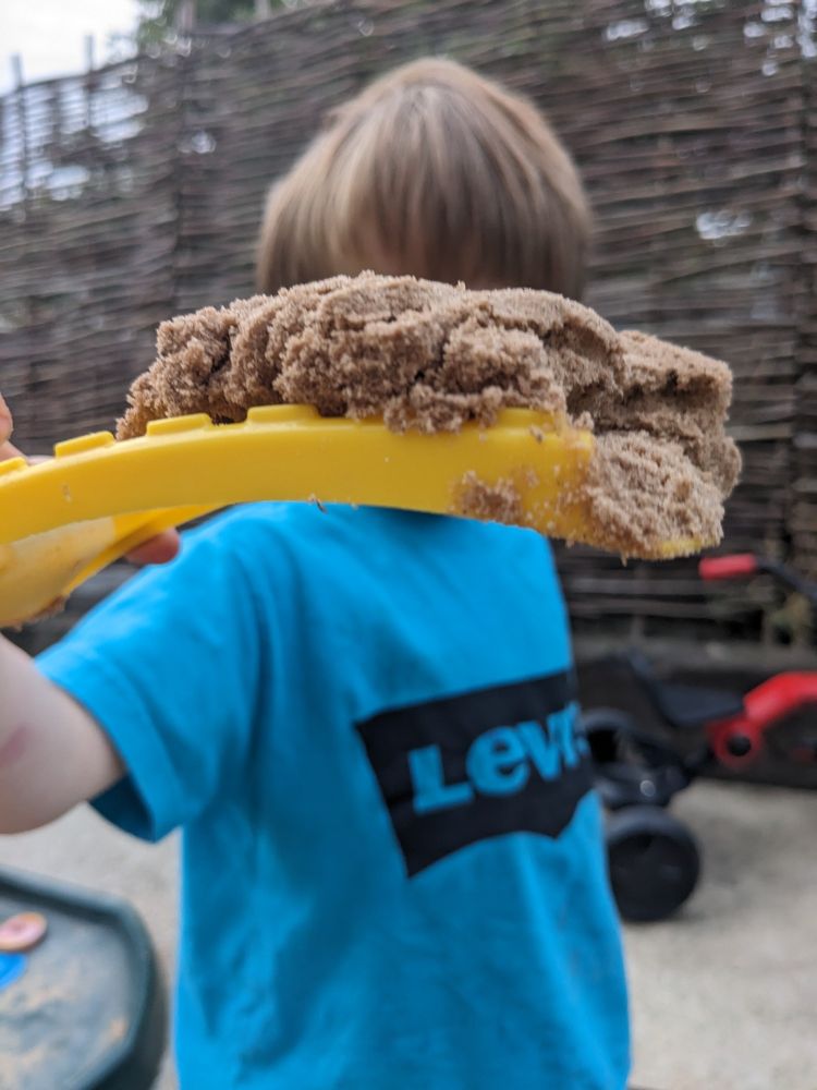 My 3 year old son holding up a pile of sand on a bit of yellow plastic
