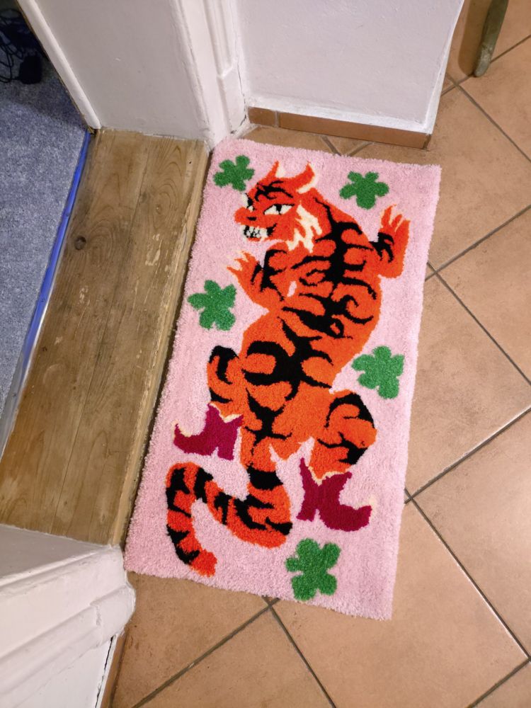 Above view of small handmade rug depicting a grinning tiger in red boots surrouded by green leaves.