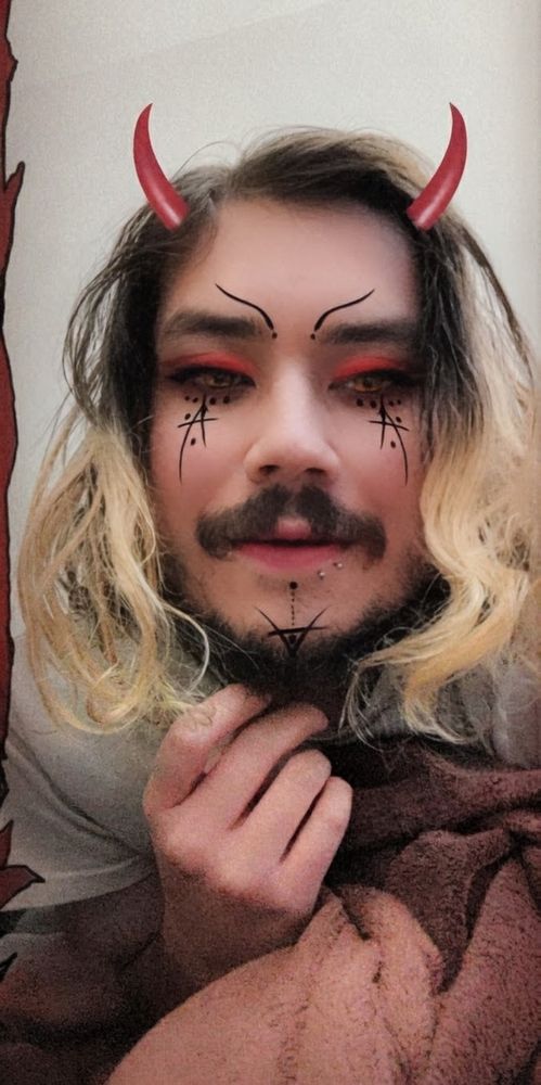 A selfie of me lying in bed smiling, with a spooky evil Snapchat filter 