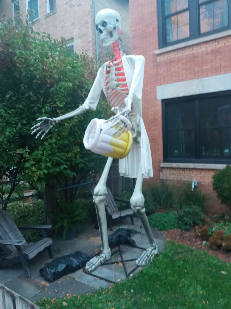 Giant yard skeleton wearing a nightie(?) and holding a big frosty mug of beer