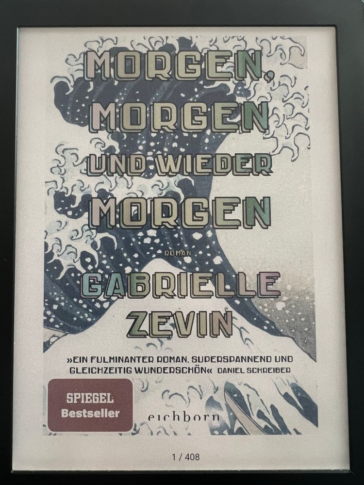 Cover des E-Books „Morgen, morgen und wieder morgen“ von Gabrielle Zevin auf einem E-Reader. Der Hintergrund zeigt eine stilisierte, japanisch anmutende Welle (angelehnt an „Die große Welle vor Kanagawa“). Der Titel ist in großen Blockbuchstaben mittig angeordnet. Unten befindet sich ein Zitat von Daniel Schreiber: „Ein fulminanter Roman, superspannend und gleichzeitig wunderschön“. Außerdem sichtbar: ein „SPIEGEL Bestseller“-Sticker und das Verlagslogo von „eichborn“. Seitenanzeige unten: „1 / 408“.