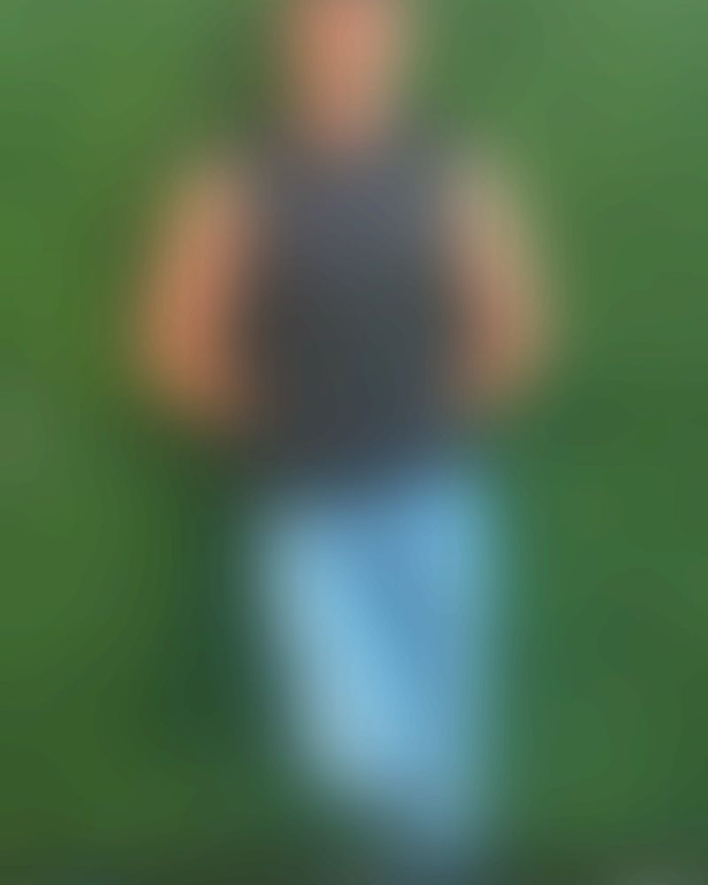 Blurred image of a man wearing blue jeans and a black sleeveless shirt on a sea of green