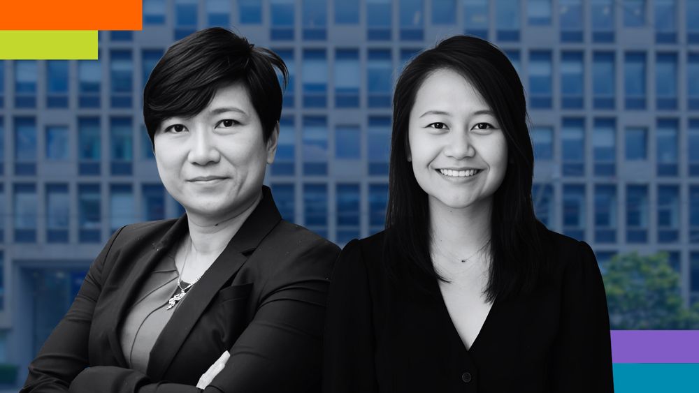 Two professional women stand in front of a modern office building, looking confident. The image is edited in black and white, except for colorful design elements in the corners, including orange, green, blue, and purple bars. The woman on the left has short hair, wears a dark blazer, and has her arms crossed, while the woman on the right has long hair and wears a black blouse, smiling warmly.