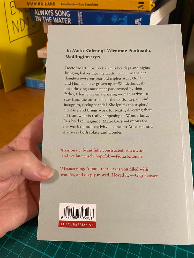 The back cover of the novel, with blurb that reads:

Te Motu Kairangi Miramar Peninsula, Wellington 1912

Doctor Matti Loverock spends her days and nights bringing babies into the world, which means her daughters-seven-year-old triplets Ada, Oona and Hanna—have grown up at Wonderland, the once-thriving amusement park owned by their father, Charlie. Then a grieving woman arrives to stay from the other side of the world, in pain and incognito, fleeing scandal. She ignites the triplets' curiosity and brings work for Matti, diverting them all from what is really happening at Wonderland.
In a bold reimagining, Marie Curie-famous for her work on radioactivity-comes to Aotearoa and discovers both solace and wonder.

Passionate, beautifully constructed, sorrowful and yet immensely hopeful. -Fiona Kidman

'Mesmerising. A book that leaves you filled with wonder, and deeply moved. I loved it. —Gigi Fenster