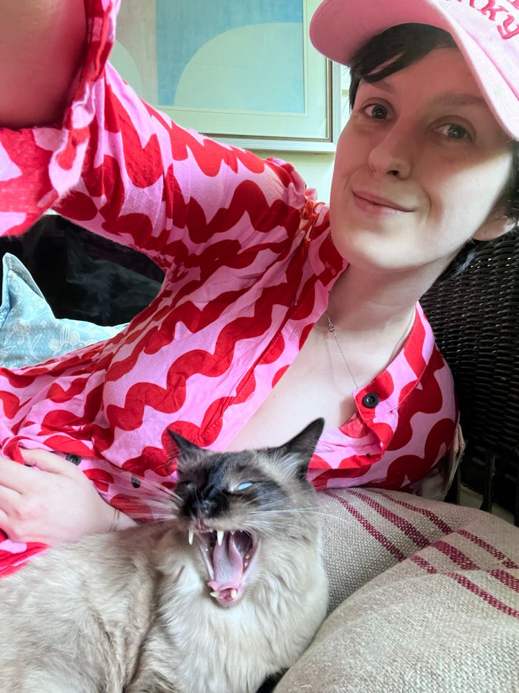 Another selfie of Aliya with her cat, Jeremy. This time, she is smiling and he is yawning and his yawn shows his fangs and makes him look ferocious.
