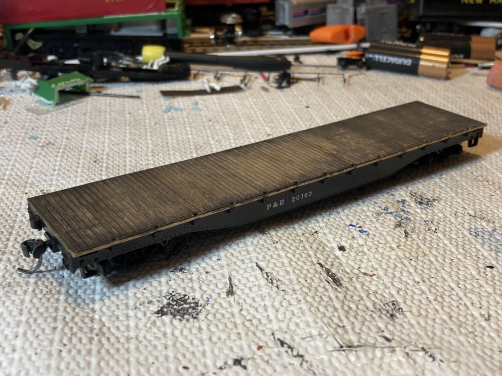 A model of a flatcar sits on a workbench. The car has been custom painted for my freelance railroad, the Poughkeepsie and Eastern, and is decorated as car # 20160. The body is painted black and the wood decking has been through a few black washes. This car went through the same process as the previous P&E flatcar # 20107.
