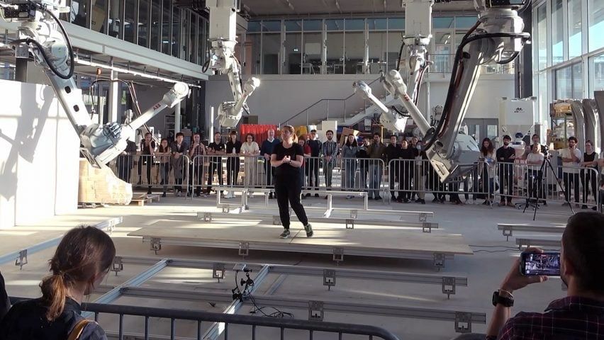 Madeline Gannon surrounded by 4 industrial robots that are following her around a factory. 