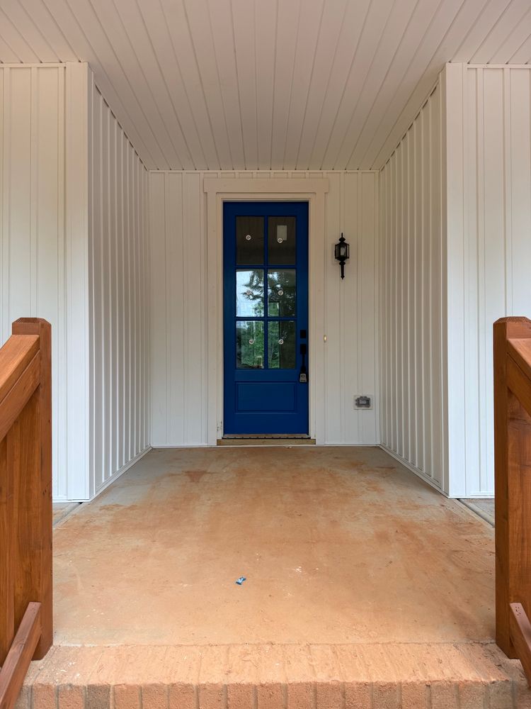 A picture of a portion of the porch of a white house with a bright blue front door