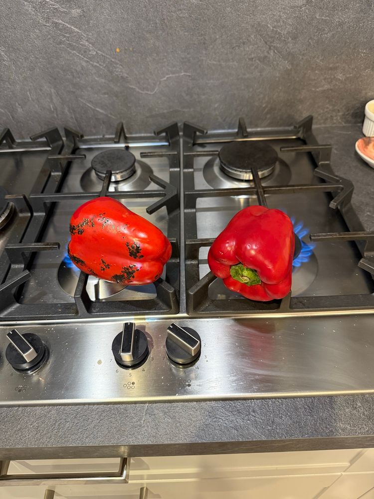 Two red peppers over an open flame on the hob.