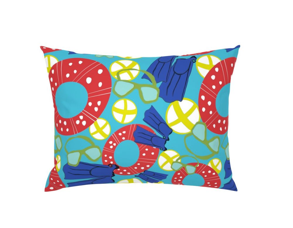 A pillow with blue fabric that has a repeating pattern of flippers, blow up red and white floaties, googles and beach balls. 