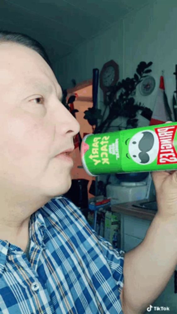 a man in a plaid shirt is drinking from a can of pringles