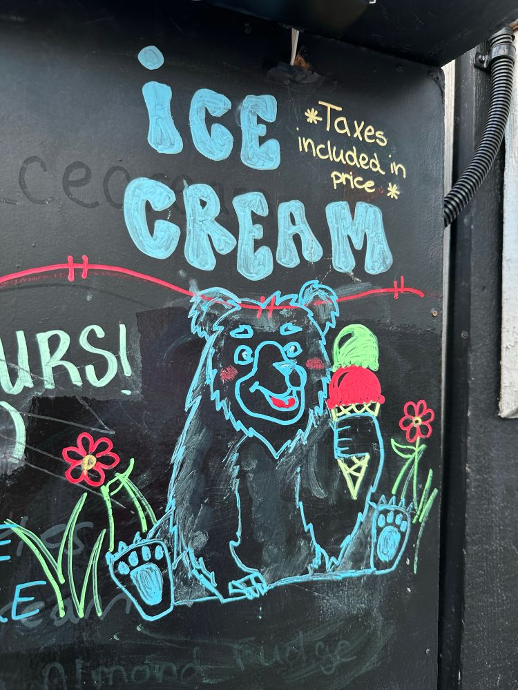 A drawing of a bear holding a cone of ice cream on a sign with the text “ice cream” and “taxes included in price” 