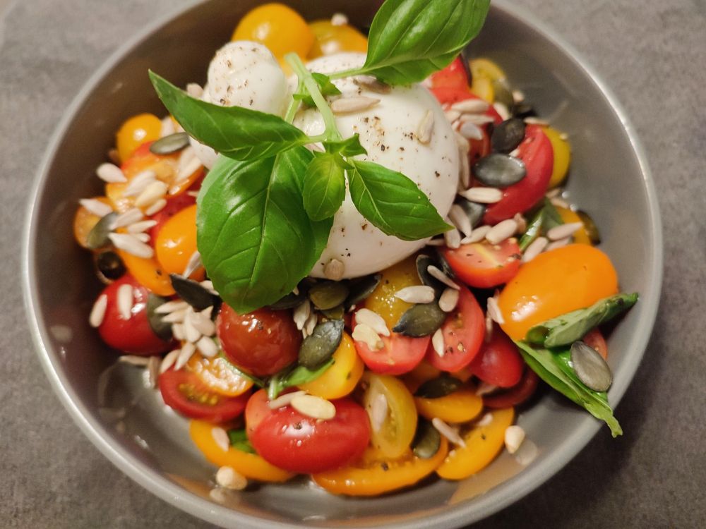 Das beschriebene Gericht angerichtet auf einem Teller. Die Kugel Burrata liegt auf dem Tomatensalat.