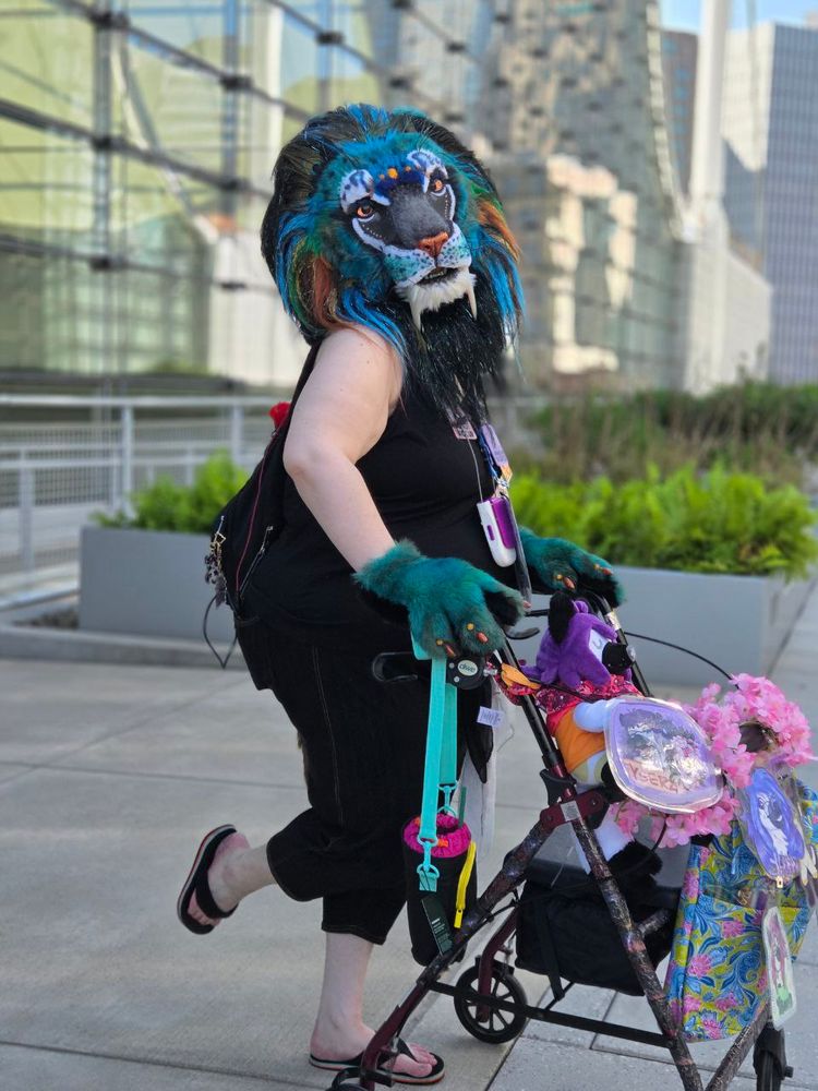 A sabertooth lioness poses for a photo. She has peacock theming and colors, and is leaning on a red rollator. She is also poodling, with exposed arms and legs because damn, it's hot.