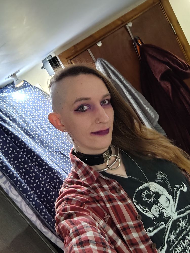 A gothy trans femme standing in front of a door 