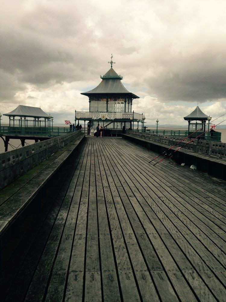 Clevedon Pier on a stormy day, a moody black and white picture with the wooden pier in the foreground and the quirky pier buildings at the end in the distance