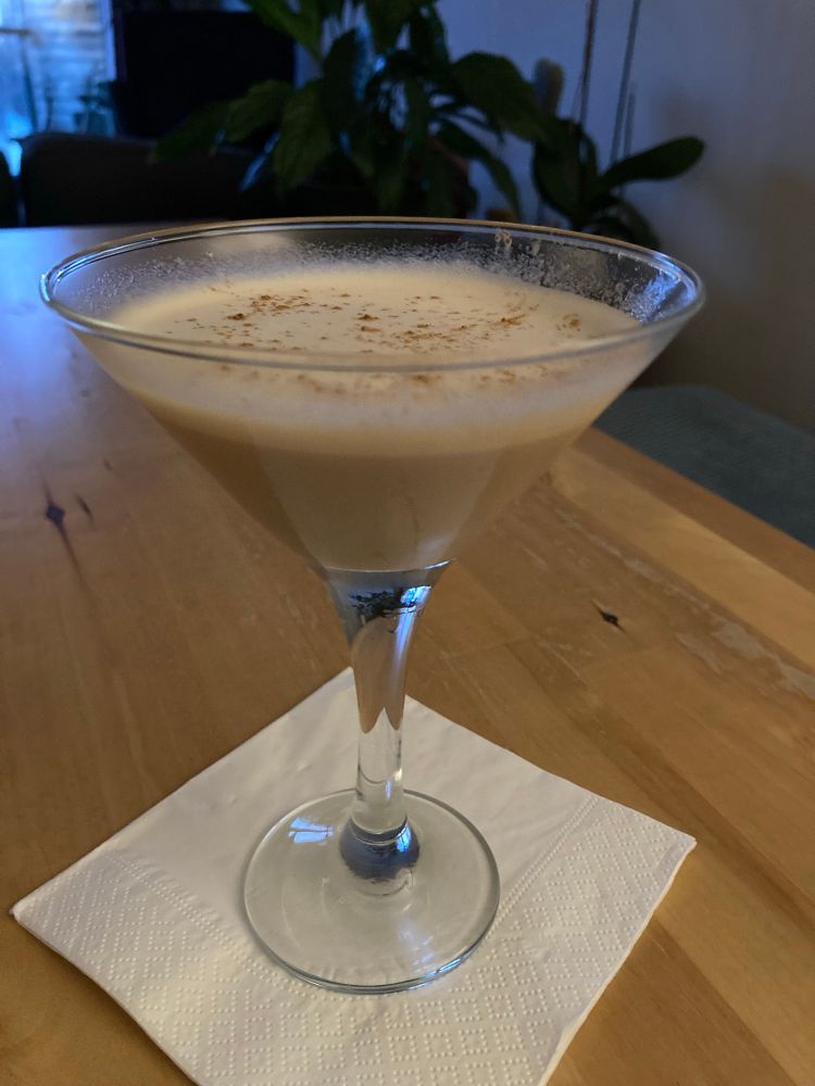 A martini glass containing a light sandy coloured drink with a creamy coloured, slightly frothy, top. It has a very light cinnamon dusting on top, although not light enough because I broke off the very small holes option of the cinnamon in a reckless fashion without considering I might want to use it one day. 