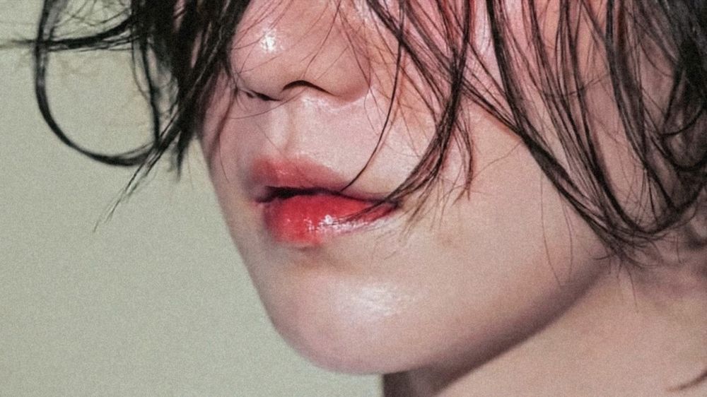 The image focus on the lower part of Yoongi's face. His skin is glossy and so his lips. His cheeks and lips are pinky. His long black hair strands are gently falling on his face. The pic is from a photoshoot and was originally posted on his Instagram (agustd).