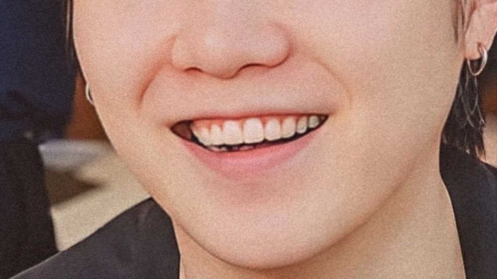 The pic focus on the lower part of Yoongi's face. He's smiling brightly showing his cute teefies. He's wearing black shirt and silver hoop earrings. The photo was originally posted on Jimin Instagram. 