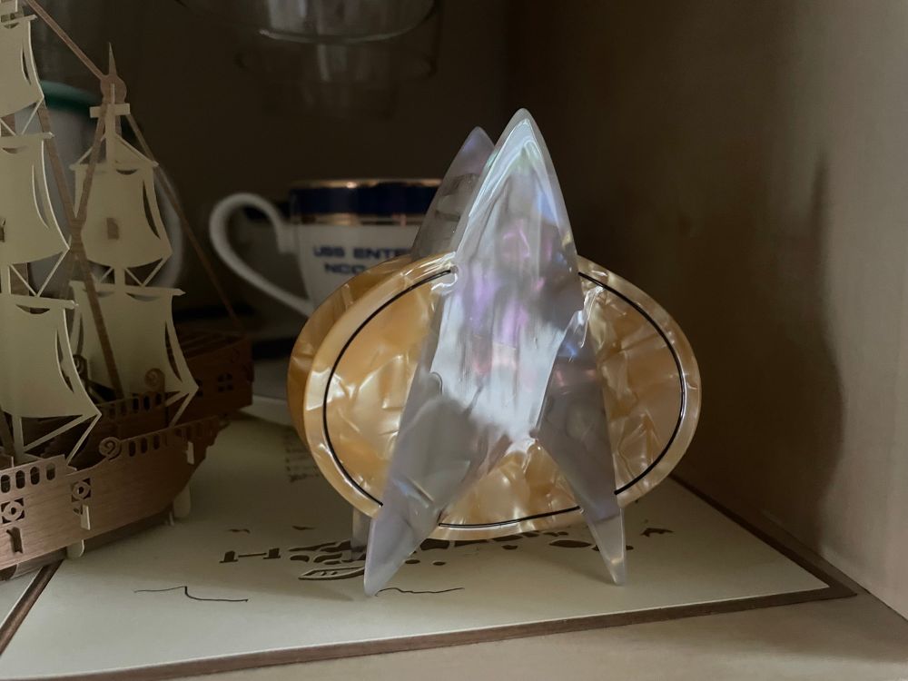 A claw hair clip shaped like the comm badge from Star Trek: The Next Generation sits on a shelf beside other trek memorabilia 