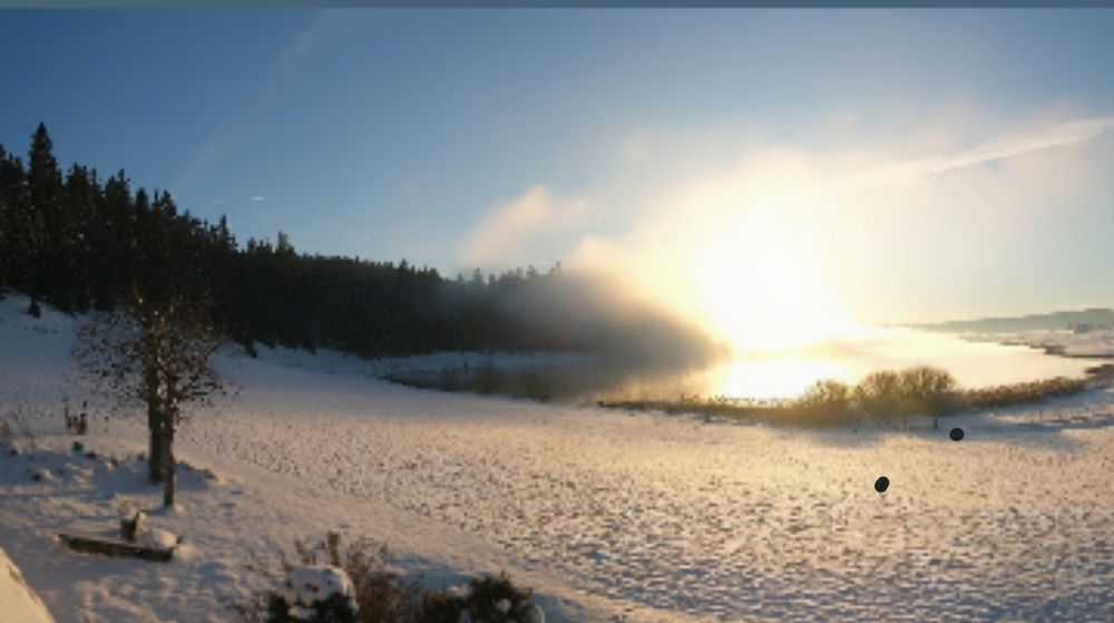 Soleil se couchant sur un lac du Jura partiellement gelé et entouré de champs blancs