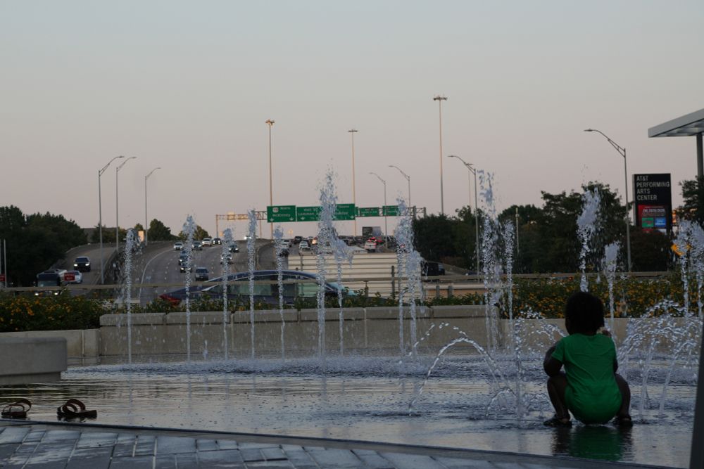 Toddler squatting in a water park looking at the 10 lane freeway on the horizon