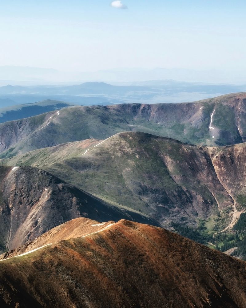 Summer scene of colorful mostly snow-free ridges under a sky made hazy from distant wildfires.