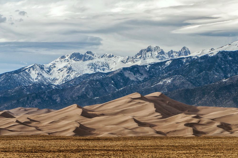 Spring views: sand dunes with high, snow covered jagged summit as a backdrop.